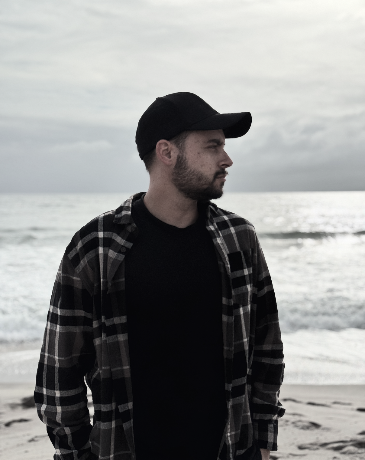 Profile photo of Theunis Hall, looking to the side on a cloudy beach, wearing a black cap and checkered shirt